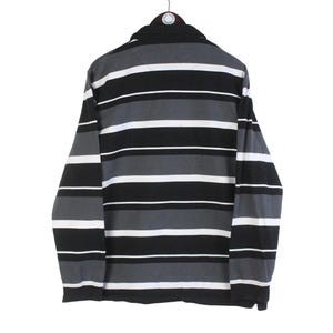 May include: A long-sleeved shirt with horizontal stripes in black, gray, and white. The shirt is hanging from a hanger and has a collared neckline. The stripes are evenly spaced across the garment.
