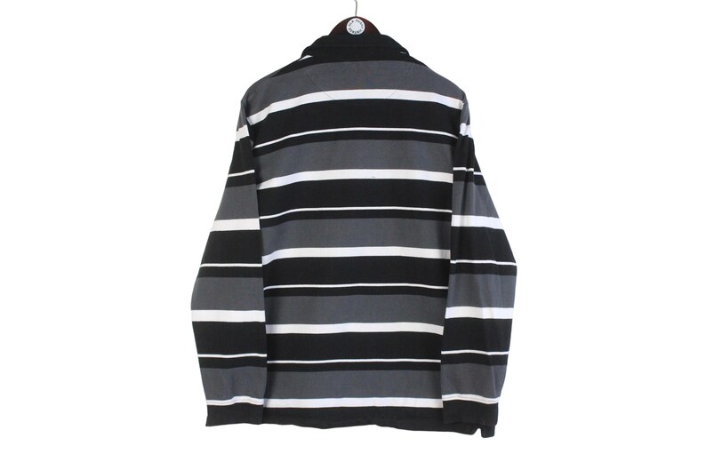 May include: A long-sleeved shirt with horizontal stripes in black, gray, and white. The shirt is hanging from a hanger and has a collared neckline. The stripes are evenly spaced across the garment.