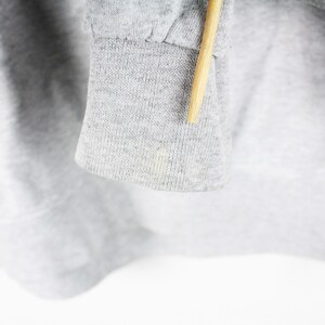 Puede incluir: Primer plano del pu&ntilde;o de tela gris de una sudadera. La tela es suave y texturizada.