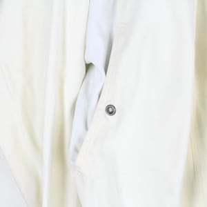 May include: A cream-colored jacket featuring a vertical zipper closure along the right side, a single visible metallic snap button on the front placket, and smooth fabric construction with clean, minimalist lines and a structured collar area.