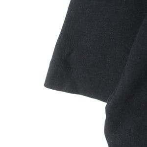 Puede incluir: Primer plano de una camiseta negra de manga corta. La tela parece ser un material de punto suave. La manga es visible, con un dobladillo limpio y una ligera curva.
