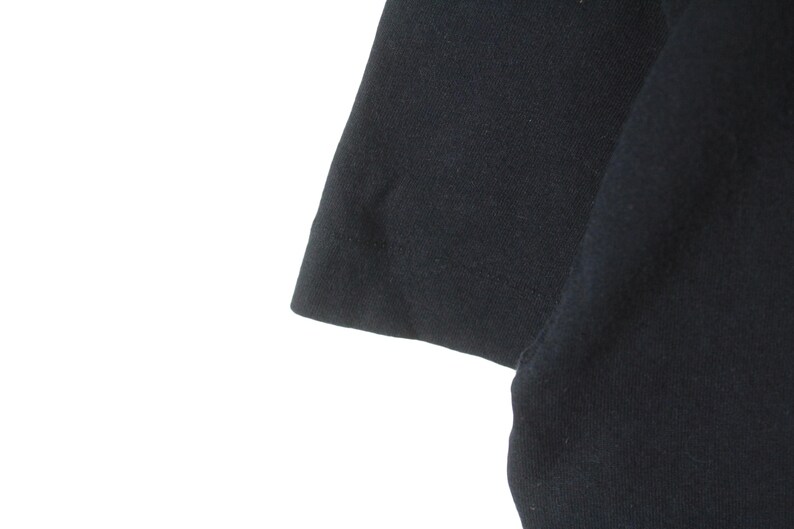 Puede incluir: Primer plano de una camiseta negra de manga corta. La tela parece ser un material de punto suave. La manga es visible, con un dobladillo limpio y una ligera curva.