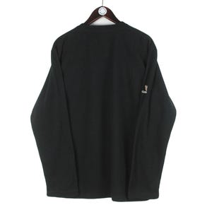 Op de afbeelding: Zwart shirt met lange mouwen hangend aan een houten kleerhanger. Het shirt heeft een klein logo op de mouw. Het shirt is gemaakt van een zacht materiaal.