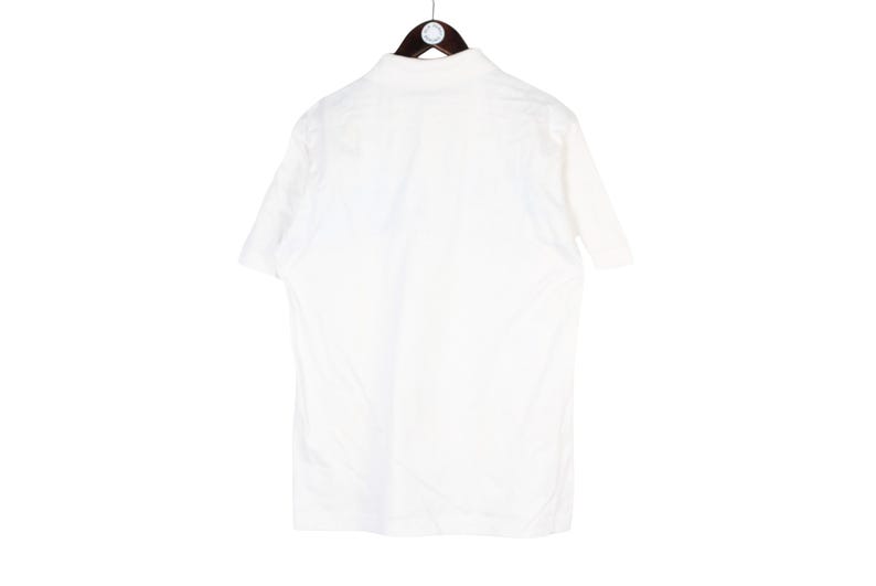 May include: A white short-sleeved polo shirt hanging on a wooden hanger. The shirt is plain and appears to be made of a lightweight fabric. The back of the shirt is visible, showing the collar and the upper back.