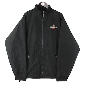 K&ouml;nnte beinhalten: Schwarze Rei&szlig;verschlussjacke mit einem Guinness-Logo auf der linken Brust. Das Logo ist in Gold, Rot und Wei&szlig;.
