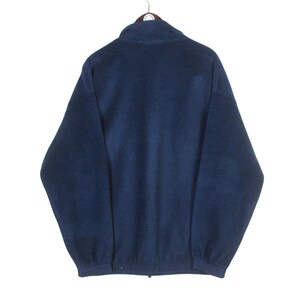 K&ouml;nnte beinhalten: Marineblaue Fleecejacke mit durchgehendem Rei&szlig;verschluss und Stehkragen. Die Jacke h&auml;ngt an einem Kleiderb&uuml;gel vor wei&szlig;em Hintergrund. Das Fleecematerial wirkt weich und warm.