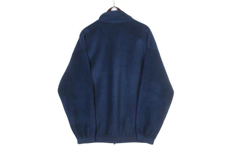 K&ouml;nnte beinhalten: Marineblaue Fleecejacke mit durchgehendem Rei&szlig;verschluss und Stehkragen. Die Jacke h&auml;ngt an einem Kleiderb&uuml;gel vor wei&szlig;em Hintergrund. Das Fleecematerial wirkt weich und warm.