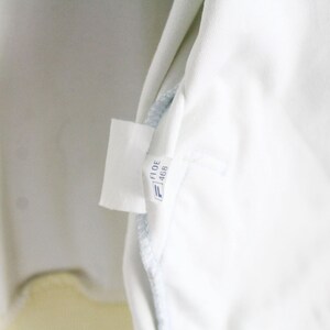 May include: A white fabric garment interior featuring a small, rectangular white care label. The label displays the text FI DE 468 in black ink, positioned above a small blue and white logo icon. The fabric appears smooth and clean.