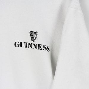 May include: White sweatshirt with the Guinness logo. The logo features a black harp and the word "Guinness" in a bold, black font. The sweatshirt is made of a soft, comfortable material.