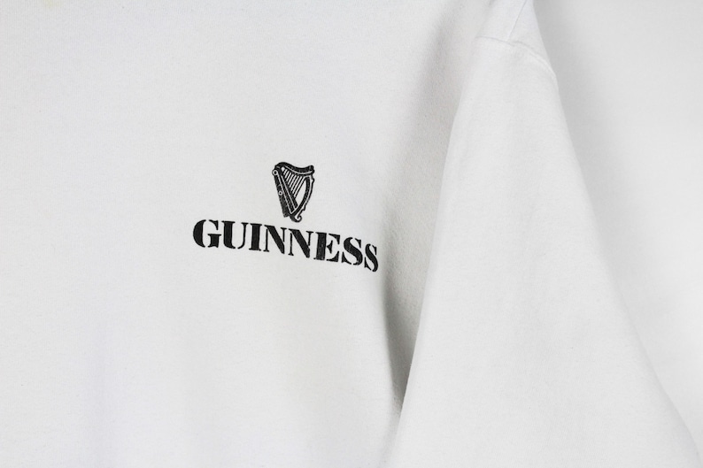 May include: White sweatshirt with the Guinness logo. The logo features a black harp and the word "Guinness" in a bold, black font. The sweatshirt is made of a soft, comfortable material.