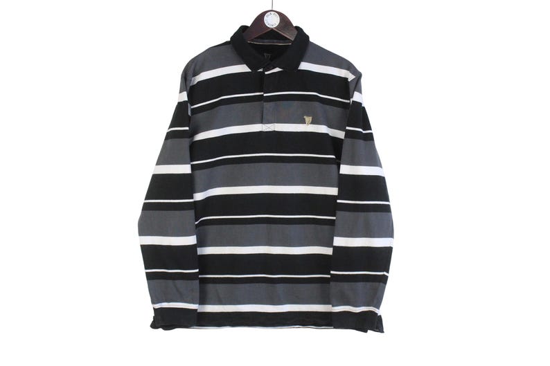 May include: Long-sleeved polo shirt with horizontal stripes in black, white, and gray. The shirt has a black collar and a small emblem on the chest. It is hanging on a wooden hanger.