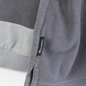 Puede incluir: Primer plano de una sudadera de forro polar gris con un dise&ntilde;o de bloques de color. La sudadera presenta un cuerpo gris oscuro, una banda gris claro y una manga gris. Una etiqueta negra con el logotipo "Guinness" est&aacute; cosida en la manga.