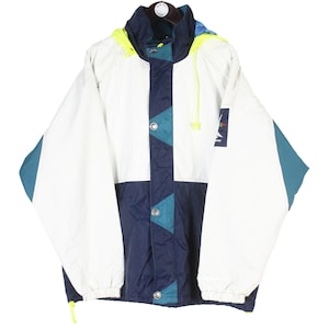 Puede incluir: Chaqueta cortavientos vintage blanca, azul marino y verde azulado. La chaqueta presenta un diseño de bloques de color con detalles en verde azulado y azul marino, una capucha y un pequeño parche con el logotipo. Cierre de cremallera.