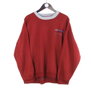 May include: Red long-sleeve sweatshirt with a grey ribbed crew neck and a small logo on the left chest. The logo is blue and white and says "Sport".