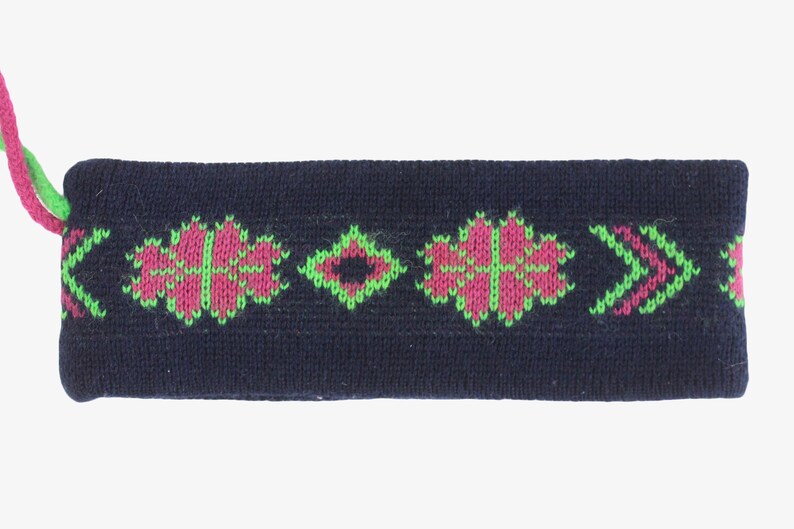 May include: A navy blue knitted headband with a floral and arrow pattern in pink and green. The headband has a matching pink and green cord attached to one end. This accessory is suitable for various activities.