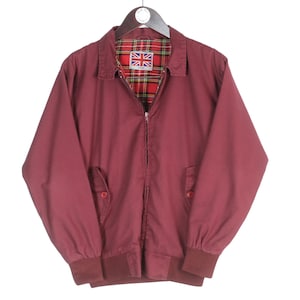 Puede incluir: Chaqueta burdeos con cremallera, cuello y dos bolsillos delanteros. La chaqueta presenta un forro de cuadros rojos y negros con un parche de la Union Jack. Los puños y la cintura son de un burdeos más oscuro.