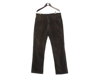 May include: Dark brown corduroy pants hanging on a black hanger. The pants have a classic five-pocket design and a button and zipper closure. The corduroy fabric has a soft, textured appearance.