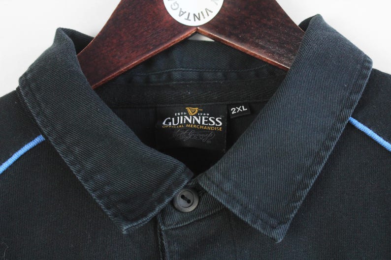 May include: Black polo shirt with a blue trim and a Guinness label that reads "Est. 1778 Dublin, Ireland, Guinness, Official Merchandise". The label also has a 2XL size tag.