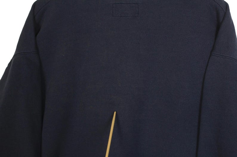 K&ouml;nnte beinhalten: Ein marineblaues Sweatshirt mit einem rechteckigen Aufn&auml;her in der N&auml;he des Halsausschnitts. Das Sweatshirt hat lange &Auml;rmel und ein schlichtes, klassisches Design, das sich f&uuml;r Freizeitkleidung eignet. Der Stoff scheint ein weiches, bequemes Material zu sein.