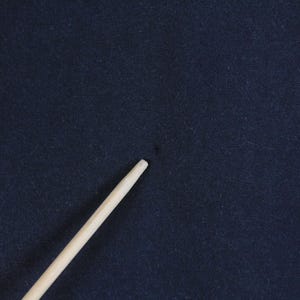 May include: A close-up of a dark navy blue fabric with a light-colored wooden stick diagonally across the frame. The fabric has a slightly textured appearance. The stick is smooth and cylindrical.