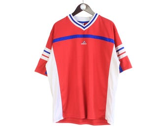 May include: Red Adidas athletic shirt with white and blue accents. The shirt has a V-neck collar with blue and white trim, and the Adidas logo is centered on the chest. The sleeves have white and blue stripes.