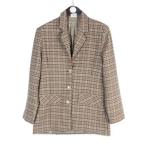 May include: A tan, brown, and black plaid blazer with a notched collar, three-button closure, and two front pockets. The blazer is hanging on a hanger against a white background. The lining is a light tan color.