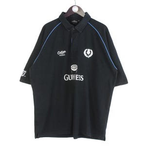 May include: Black polo shirt with blue trim and a white Guinness logo. The shirt has a small white logo that says "Cotton Traders" on the left chest.
