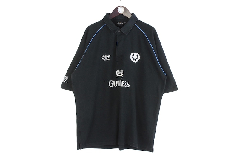 May include: Black polo shirt with blue trim and a white Guinness logo. The shirt has a small white logo that says "Cotton Traders" on the left chest.