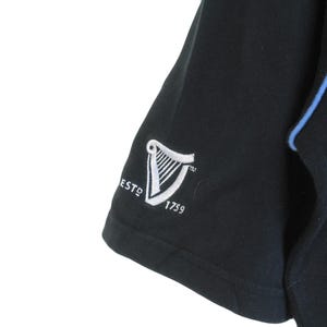 May include: Black short-sleeved shirt with a blue trim and a white embroidered Guinness logo that says "ESTD 1759"