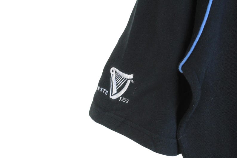 May include: Black short-sleeved shirt with a blue trim and a white embroidered Guinness logo that says "ESTD 1759"
