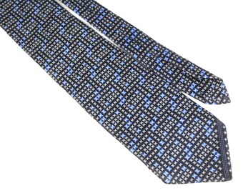 May include: A patterned necktie with a repeating geometric design in black, light blue, and white. The tie is angled across a white background, showcasing its intricate pattern and color scheme. The tie's texture appears smooth.