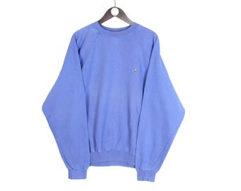 May include: A light blue sweatshirt with a small embroidered emblem on the chest. The long-sleeved top is made of a soft material and has a crew neck and ribbed cuffs and hem. The garment is hanging on a wooden hanger.