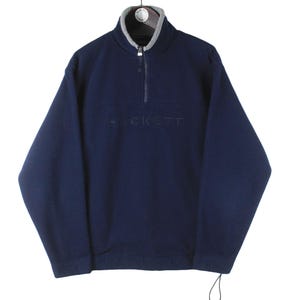 Puede incluir: Una sudadera de polar azul marino con cierre de cremallera a la mitad y la palabra "JACKETT" bordada en la parte delantera.