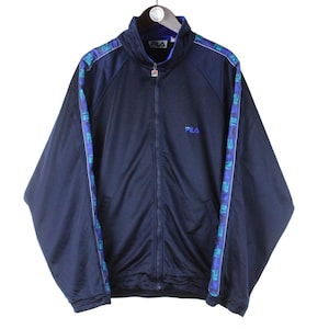Puede incluir: Una chaqueta azul marino con cremallera con un ribete estampado en azul y verde. La chaqueta tiene un logotipo de Fila en el pecho izquierdo.