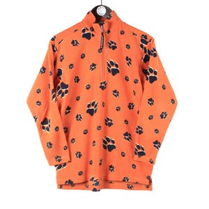 Puede incluir: Sudadera de forro polar naranja con cierre de cremallera de media cremallera y estampado de huellas de patas.