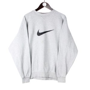 Puede incluir: Una sudadera gris con un logotipo de Nike swoosh negro en la parte delantera.