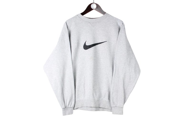 Puede incluir: Una sudadera gris con un logotipo de Nike swoosh negro en la parte delantera.