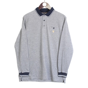 May include: A long-sleeved gray polo shirt with a navy blue collar, cuffs, and sleeve trim. The shirt has a three-button placket and a small pocket on the chest with a gold emblem. The shirt is hanging on a wooden hanger.