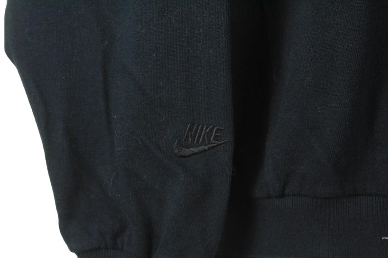 Może przedstawiać: Czarna bluza z długim rękawem z haftowanym logo Nike na lewej piersi.