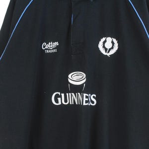 May include: Black rugby jersey with blue trim, featuring a white "Cotton Traders" logo, a white Guinness logo with a pint glass graphic, and a white thistle emblem.
