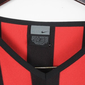 Puede incluir: Camiseta con cuello en V a rayas negras y rojas con una etiqueta con el logo de Nike. La camiseta tiene una etiqueta con informaci&oacute;n de tallas. La camiseta est&aacute; hecha en Tailandia.