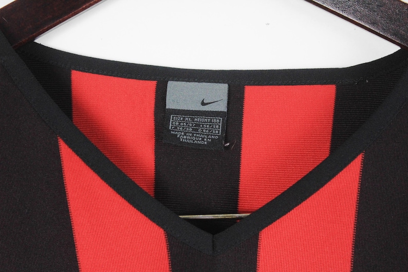 Puede incluir: Camiseta con cuello en V a rayas negras y rojas con una etiqueta con el logo de Nike. La camiseta tiene una etiqueta con informaci&oacute;n de tallas. La camiseta est&aacute; hecha en Tailandia.