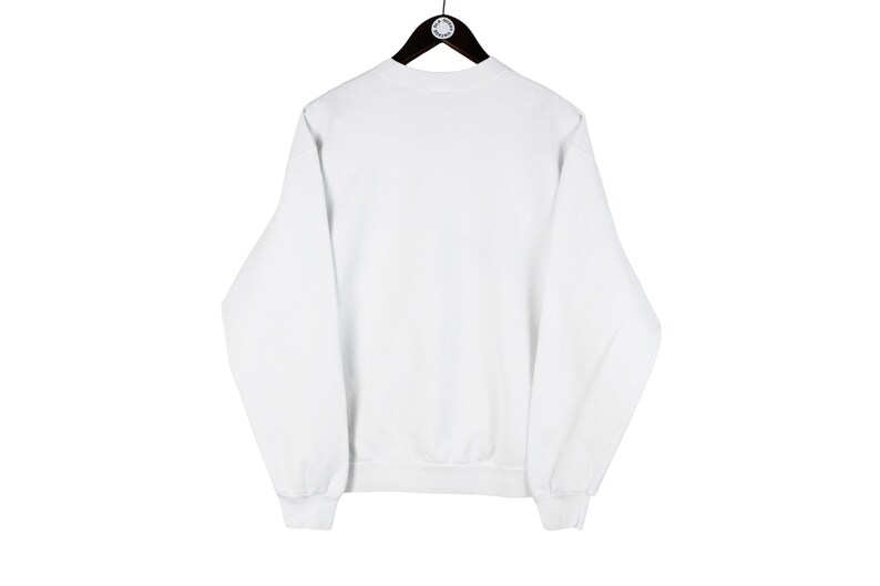 May include: A plain white sweatshirt with long sleeves, a crew neck, and ribbed cuffs and hem. The sweatshirt is hanging on a black hanger against a white background. The garment is a casual style.
