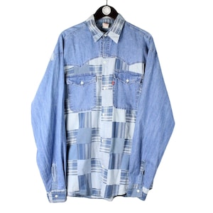 May include: A long-sleeve button-down shirt featuring a light blue denim yoke and sleeves combined with a central patchwork panel of various blue and white plaid patterns. The shirt includes two chest pockets with flaps and a small red brand tag.