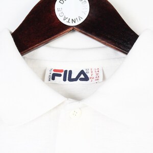 May include: A white ceramic mug with a black handle and the text "But First, Coffee" in a bold, black font. The mug is sitting on a wooden surface. The mug is approximately 4 inches tall.