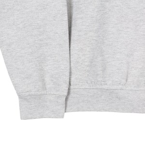 Puede incluir: Primer plano de una sudadera gris claro. La imagen muestra el pu&ntilde;o de la manga y el dobladillo inferior de la sudadera. La tela parece ser un material de punto suave. La sudadera es de color s&oacute;lido.