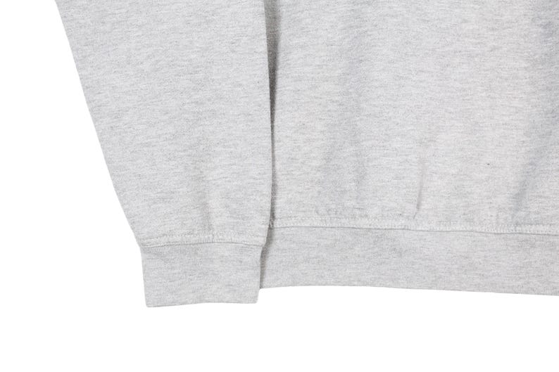 Puede incluir: Primer plano de una sudadera gris claro. La imagen muestra el pu&ntilde;o de la manga y el dobladillo inferior de la sudadera. La tela parece ser un material de punto suave. La sudadera es de color s&oacute;lido.