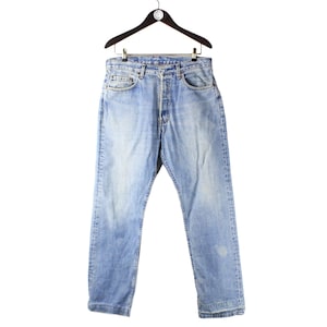 May include: Light blue denim jeans featuring a classic five-pocket design, a button fly closure, and a faded wash finish. The jeans are displayed on a black hanger, showcasing a straight-leg cut with visible whiskering and light distressing.