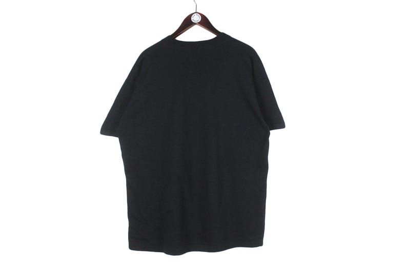 Op de afbeelding: Een zwart T-shirt met korte mouwen hangt aan een houten hanger. Het shirt is effen en lijkt van een zacht materiaal te zijn. De achtergrond is wit.