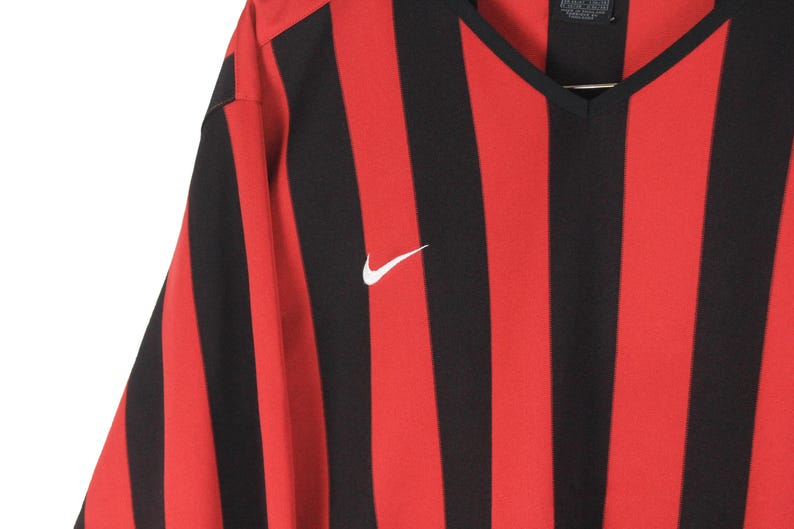 Puede incluir: Camiseta deportiva a rayas rojas y negras con cuello en V. La camiseta presenta un logotipo blanco de Nike en el pecho. La tela tiene un patr&oacute;n de rayas verticales.